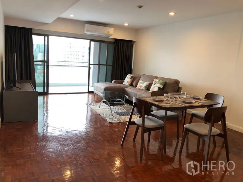 Condominium for rent or sale in Sathon, Bangkok - Bright living and dining area with L-shaped sofa, set table, TV stand and sliding doors to a balcony with city view.