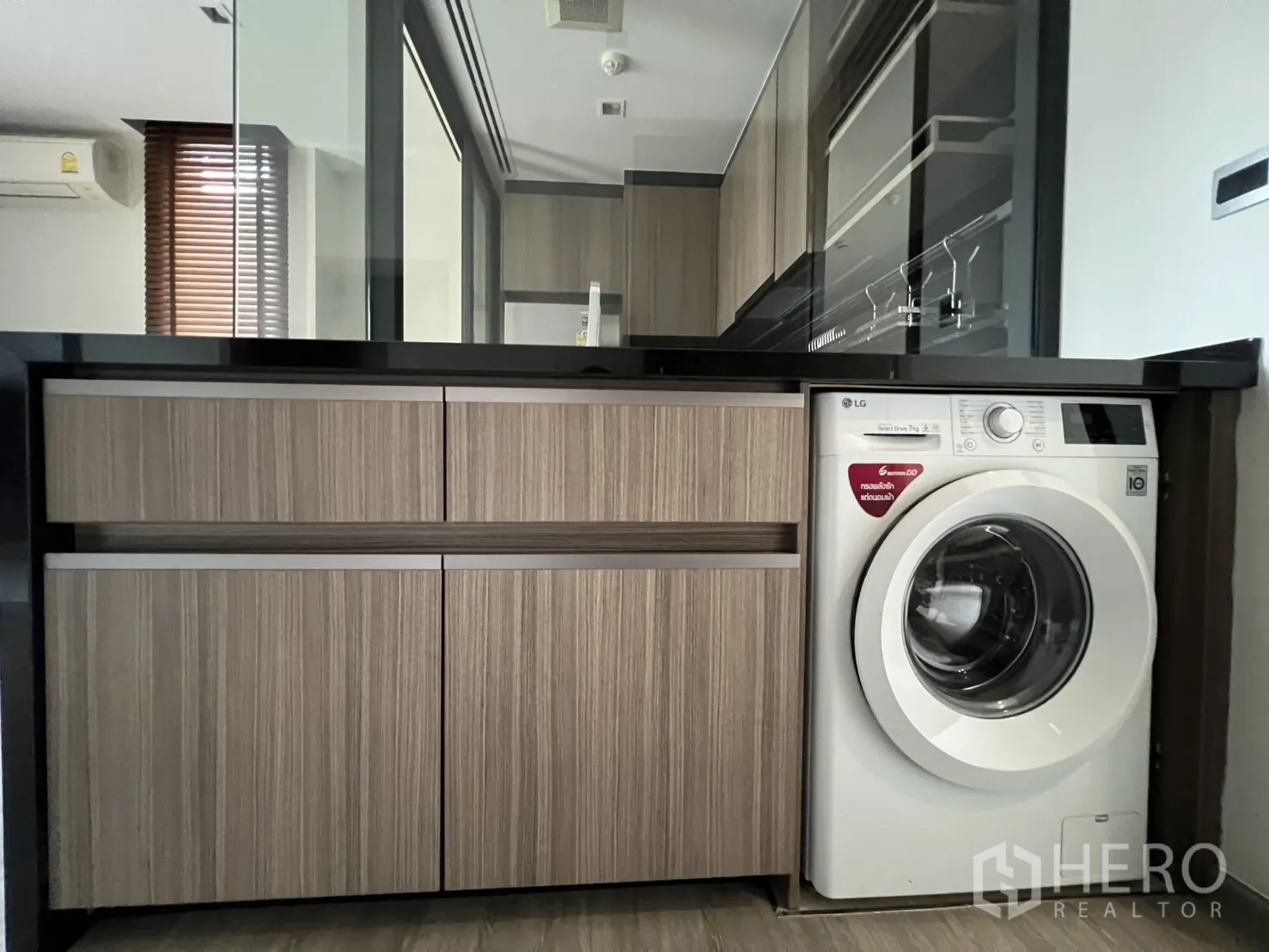 Condominium for rent in Watthana, Bangkok - Close-up of a kitchen with black countertop, wood cabinets, and a front-loading washing machine.