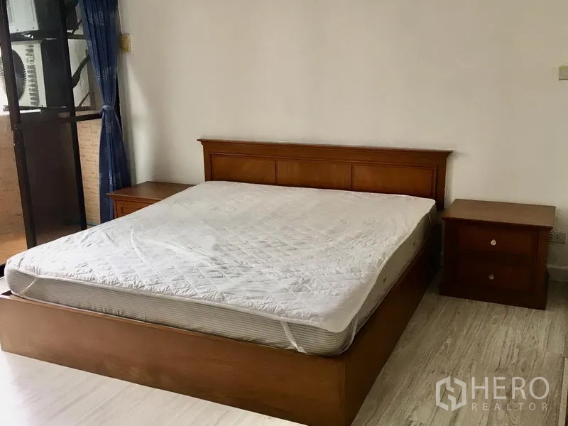 Condominium for rent in Watthana, Bangkok - Master bedroom with wooden bed frame, bedside tables and sliding door opening to a balcony.