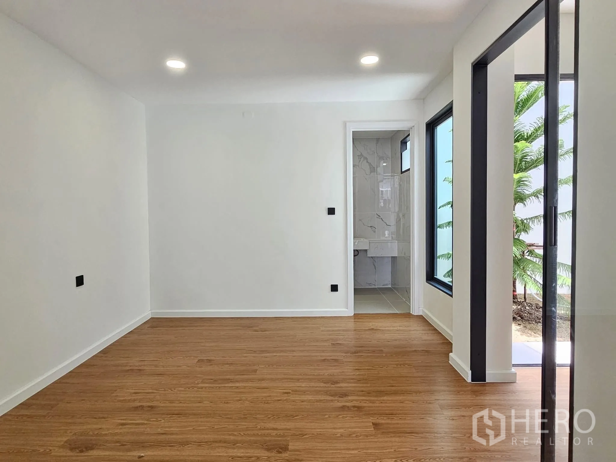 บ้านเดี่ยว for sale in Lat Phrao, Bangkok - ห้องชั้นล่างพื้นลายไม้ มีประตูเข้าห้องน้ำและหน้าต่างมองเห็นสวน