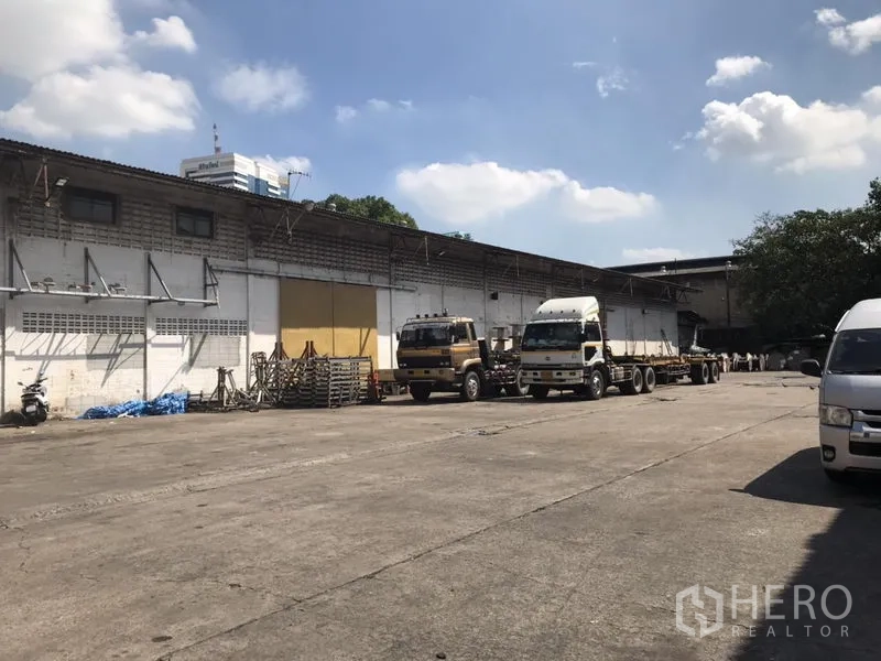 货栈 出租在Khlong Toei, Bangkok - 宽阔的混凝土场地，卡车停靠在带装卸雨棚的单层仓库前