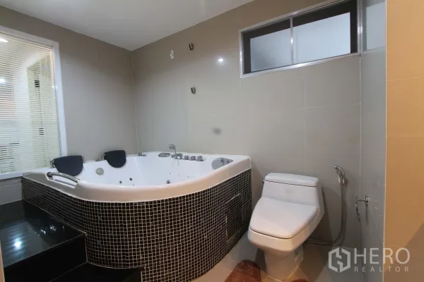 Condominium for rent in Watthana, Bangkok - Modern bathroom with corner Jacuzzi bathtub, tiled walls, and toilet.