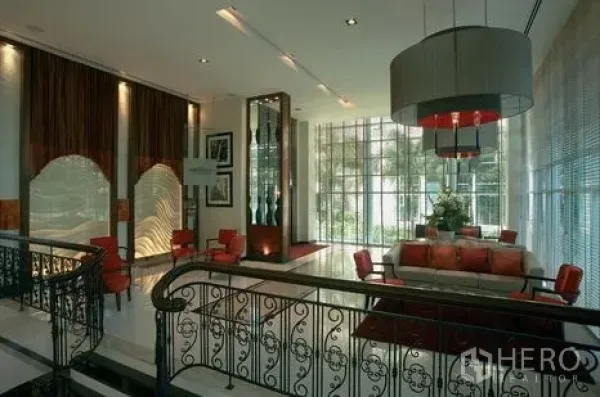 Condominium for rent or sale in Khlong Toei, Bangkok - Elegant condominium lobby with high ceilings, floor-to-ceiling windows, red sofas, and decorative railing.