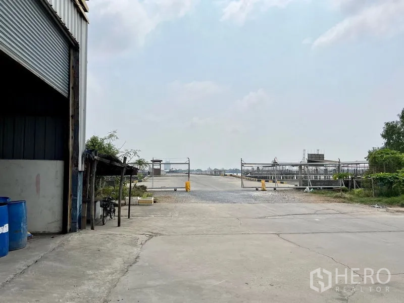 Warehouse for rent in Phra Samut Chedi, Samut Prakan - Wide loading yard facing a secure gate and internal road within an industrial compound.