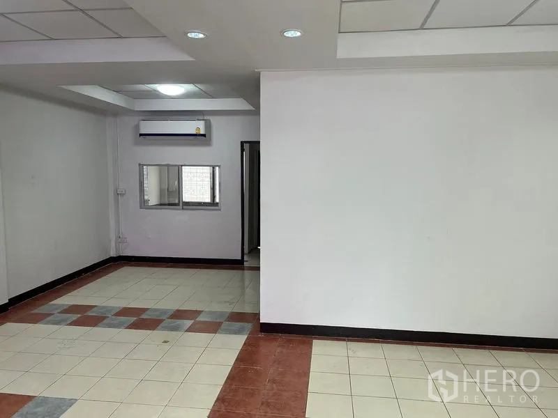 Townhouse for rent in Khlong Toei, Bangkok - Tiled living area with white walls, recessed ceiling lights and wall-mounted air conditioner.