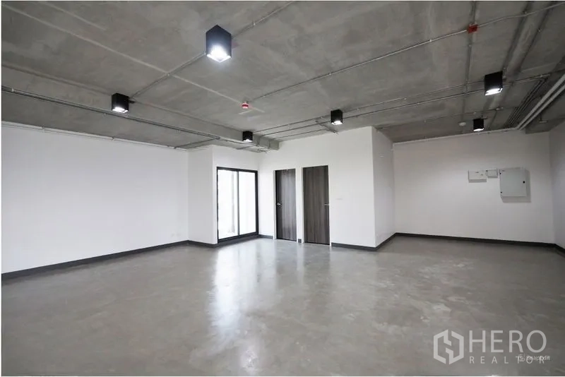 Office Space for rent in Watthana, Bangkok - Spacious office interior with exposed ceiling, concrete floor, two wood doors, and a sliding glass door.