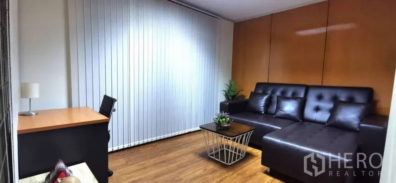 Home Office for rent in Khlong Toei, Bangkok - Executive office area with black leather sofa, wood flooring, vertical blinds, and a compact desk.