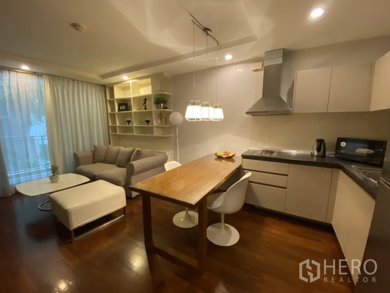 คอนโด ให้เช่าหรือขายในKhlong Toei, Bangkok - ห้องนั่งเล่นแบบเปิดโล่ง พื้นไม้ ชั้นวางบิลต์อิน โซฟาสีเทา และครัวรูปตัวแอลพร้อมฮูดสแตนเลสและโคมไฟแขวน