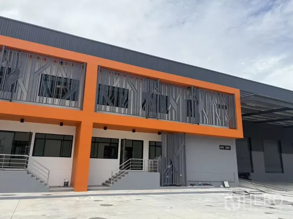 Factory for rent in Bang Pakong, Chachoengsao - Newly built factory facade with bold orange upper floor, metal screens, and office entrances with stairways.