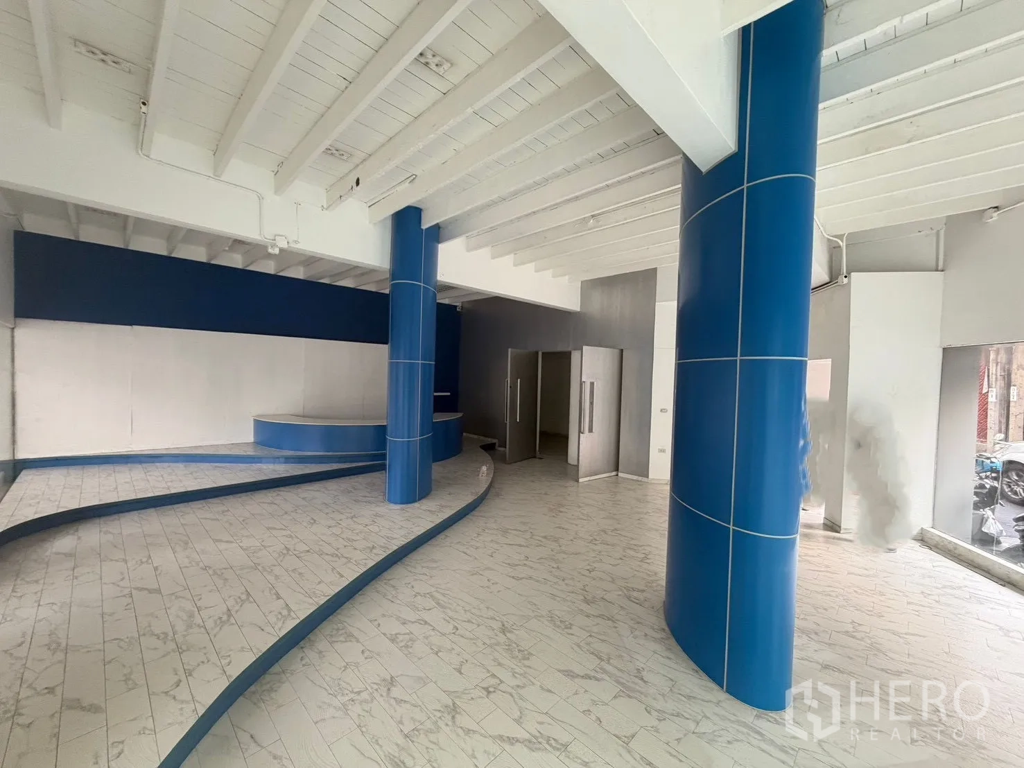 Shophouse for rent in Watthana, Bangkok - Wide showroom space with blue columns and a curved display platform.