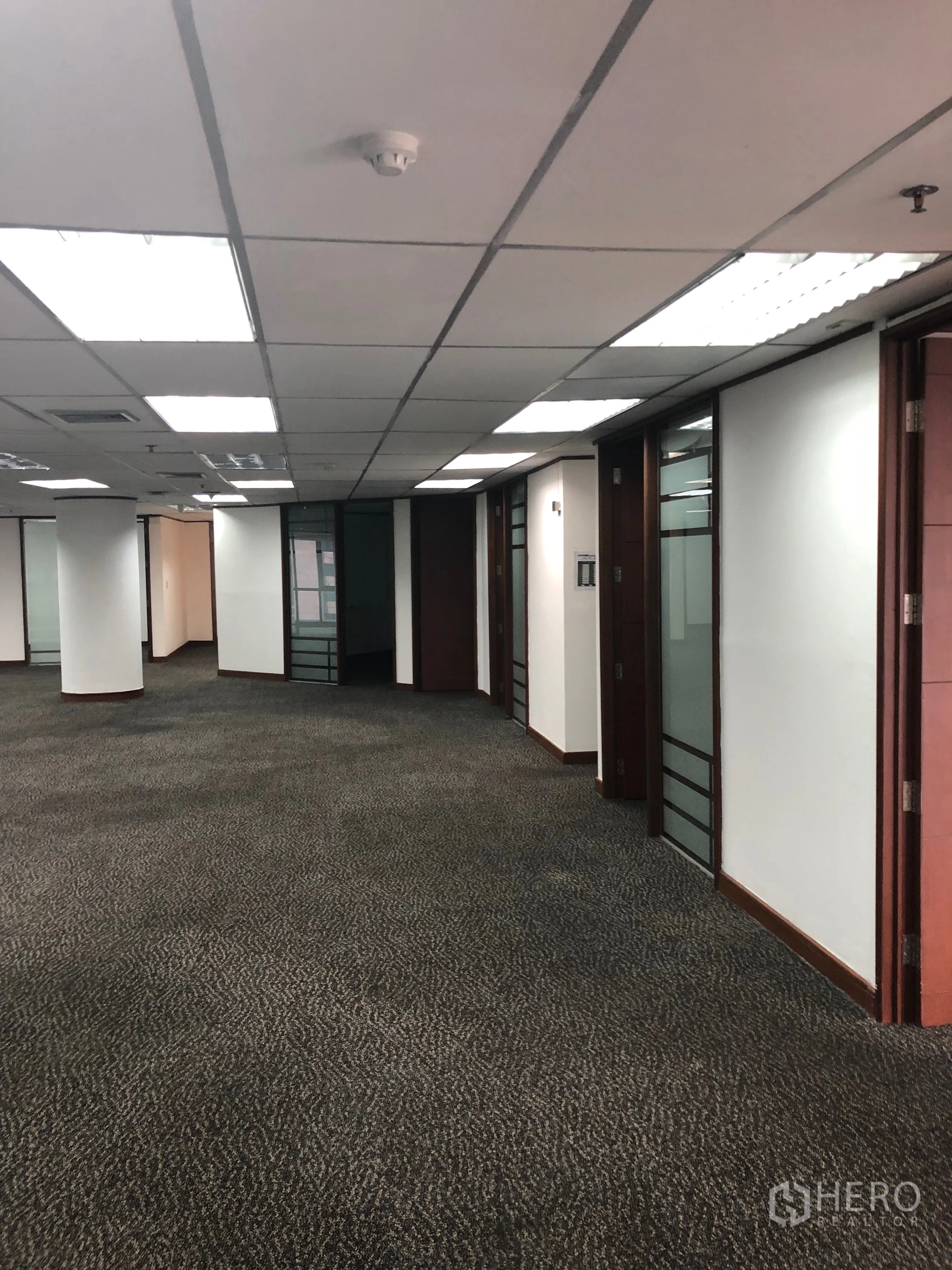 Office Space for rent in Khlong Toei, Bangkok - Hallway view of the office with multiple glass doors, wood trim and bright ceiling lighting.