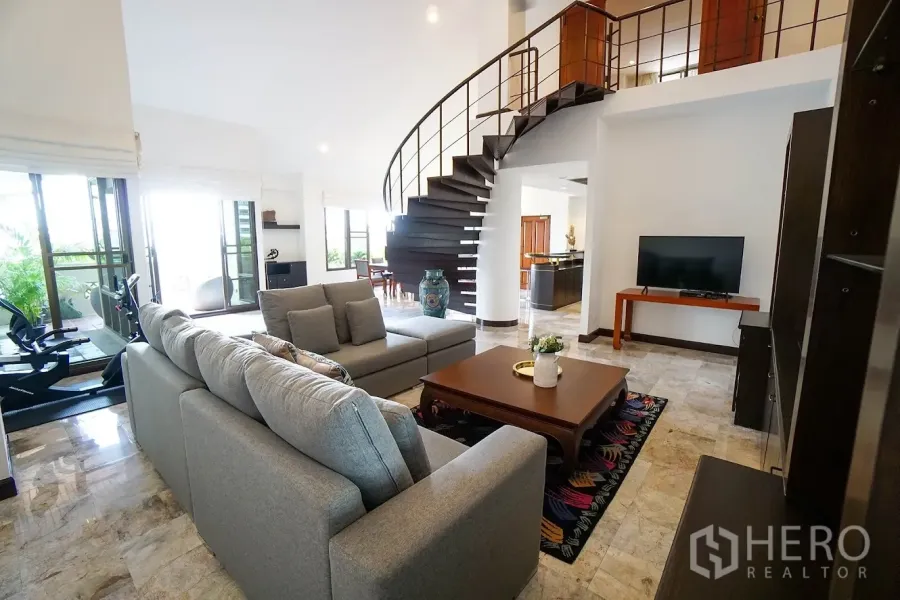 房间 出租在Watthana, Bangkok - 采光充足的客厅，灰色转角沙发、电视与旋转楼梯。