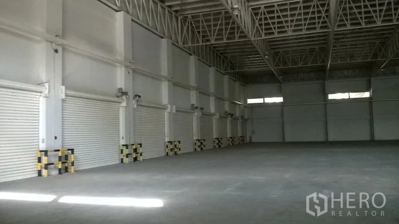 Warehouse for rent in Bang Sao Thong, Samut Prakan - Spacious warehouse interior with steel truss roof and shutter doors.
