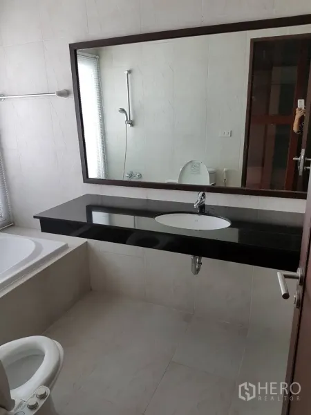 Condominium for rent or sale in Watthana, Bangkok - Bright bathroom with large mirror, black stone vanity, bathtub, and toilet.