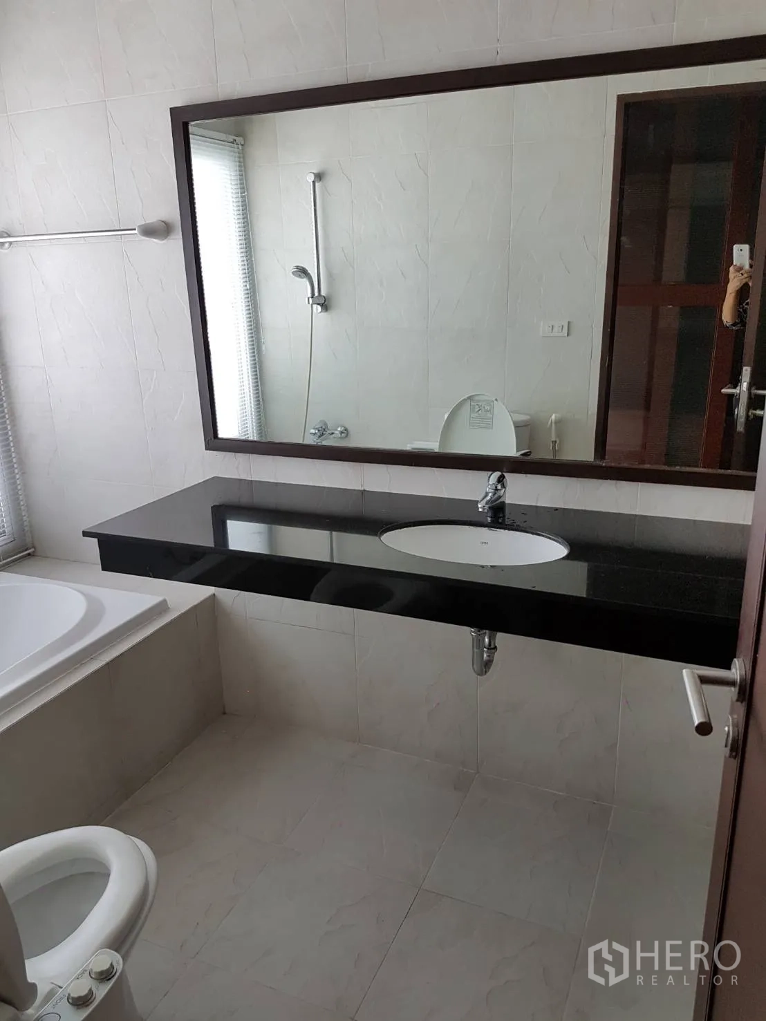 Condominium for rent or sale in Watthana, Bangkok - Bright bathroom with large mirror, black stone vanity, bathtub, and toilet.
