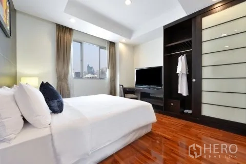 Apartment for rent in Watthana, Bangkok - Cozy bedroom with large window, TV console, and sliding-door wardrobe.