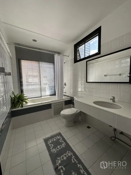 公寓 出租在Khlong Toei, Bangkok - 白色瓷砖浴室，带浴缸、洗手台和采光窗。