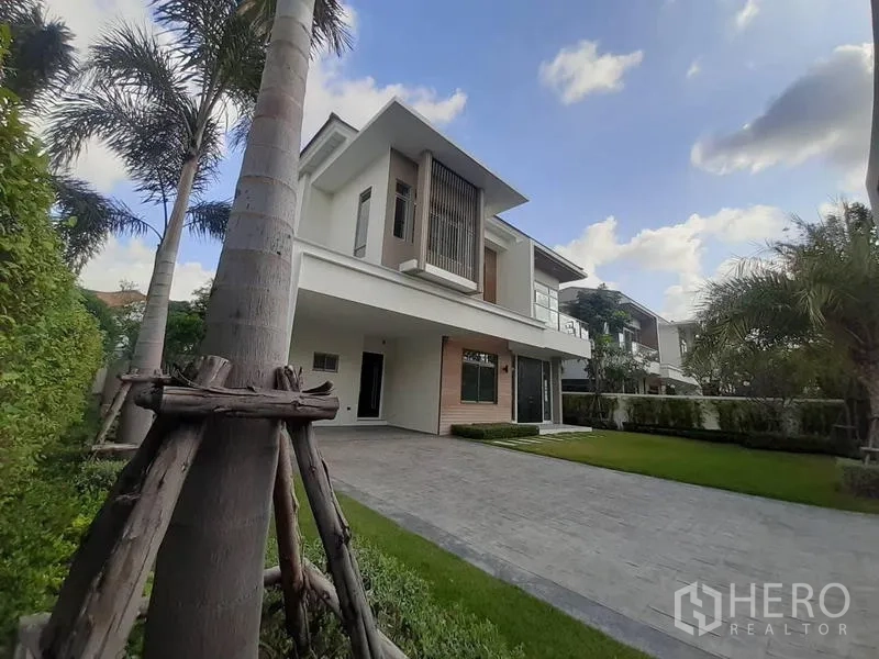 Detached House for rent in Bang Phli, Samut Prakan - Modern two-storey detached house with a wide driveway, manicured lawn and palm trees.