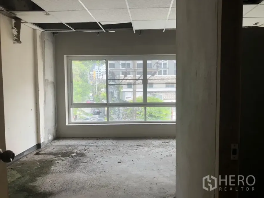 Townhouse for rent in Watthana, Bangkok - Unfinished room with a large window, city views, exposed ceiling tiles, and a concrete floor.