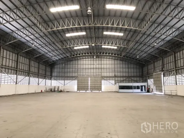 Warehouse for rent in Pathum Thani - Expansive clear-span warehouse interior with a high arched steel truss roof and smooth concrete floor.