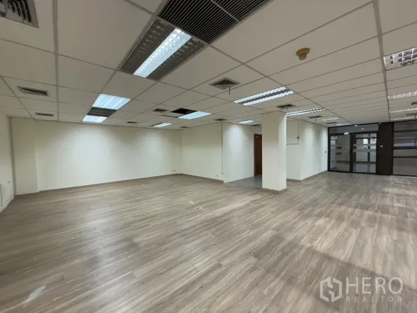 办公空间 出租在Chatuchak, Bangkok - 开放式办公室，带立柱、格栅吊顶与日光灯，木纹地面及玻璃入口。