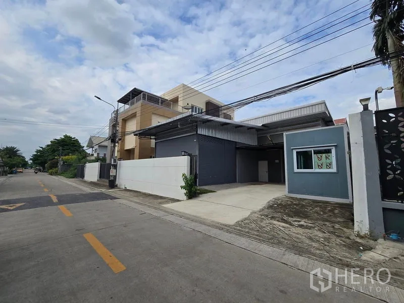 Warehouse for rent in Don Mueang, Bangkok - Angled view showing wide road access and a concrete driveway to the warehouse roller shutter.
