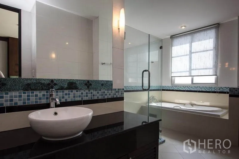 Condominium for rent in Khlong Toei, Bangkok - Modern bathroom featuring a vessel sink with mosaic backsplash, glass shower, and bathtub beside a bright window.