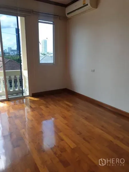 Townhouse for rent in Bang Kho Laem, Bangkok - Sunlit bedroom with polished wood floor, air conditioner and balcony access with city view.