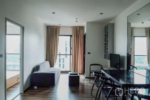 公寓 出租在Khlong Toei, Bangkok - 明亮客厅，灰色沙发、落地窗与镜面墙的曼谷公寓内部。