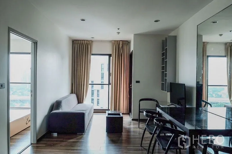 公寓 出租在Khlong Toei, Bangkok - 明亮客厅，灰色沙发、落地窗与镜面墙的曼谷公寓内部。