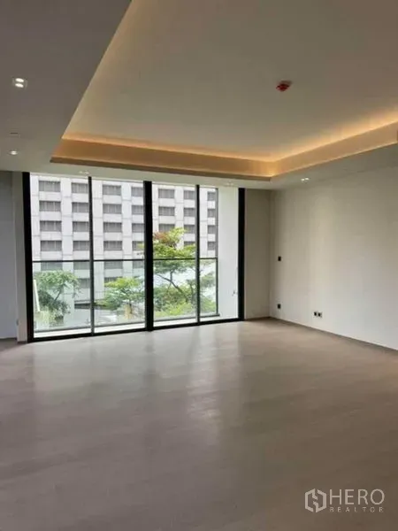 Condominium for rent in Pathum Wan, Bangkok - Bright living area with floor-to-ceiling windows and leafy city views.