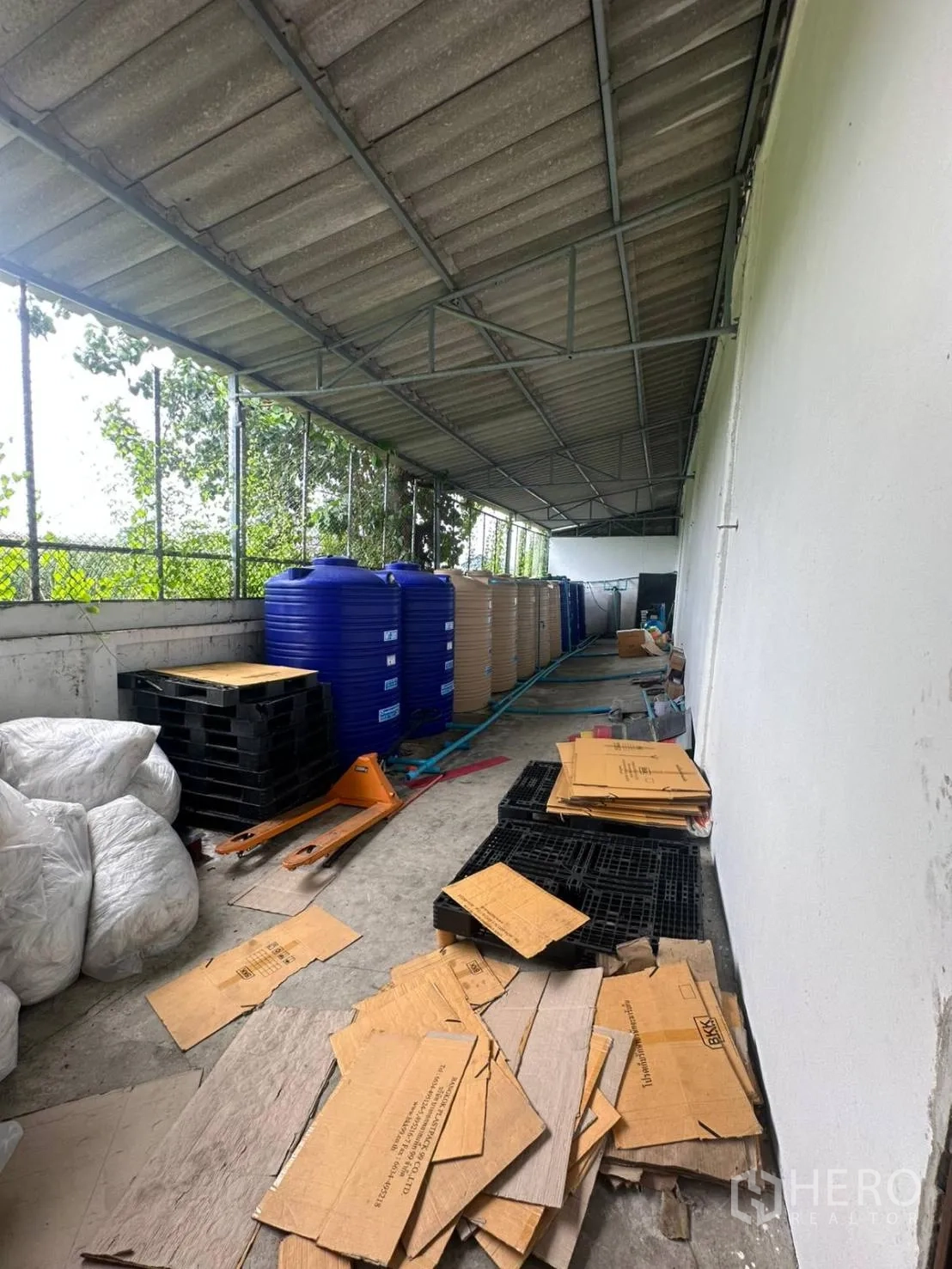 Factory for rent in Bang Phli, Samut Prakan - Covered side yard for storage with corrugated roof, pallets and large water tanks.