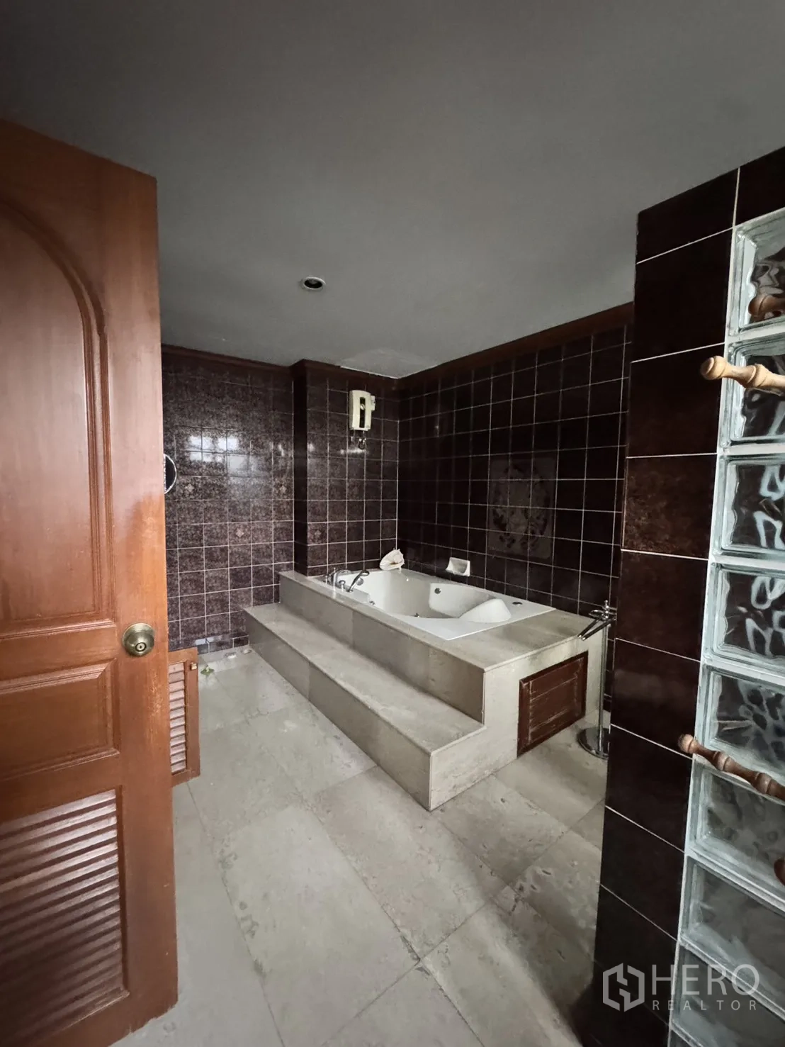 Home Office for rent in Watthana, Bangkok - Bathroom with step-up bathtub, dark brown wall tiles, and glass-block partition.