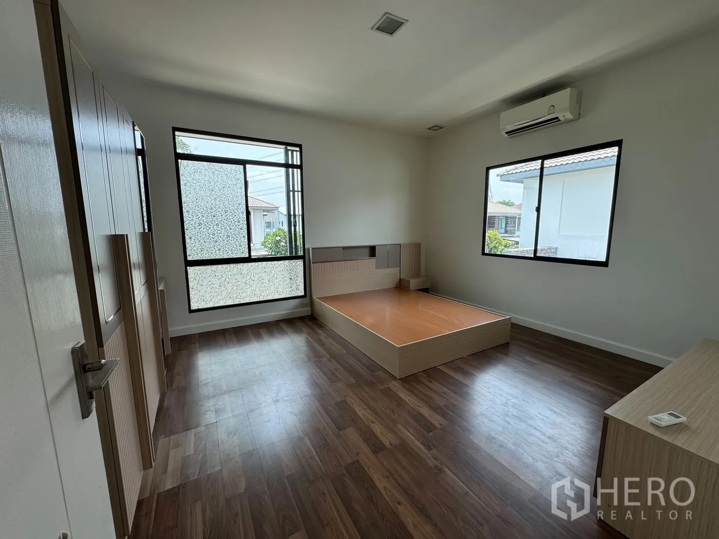 Detached House for rent in Prawet, Bangkok - Bright bedroom with two windows, wood floors and a platform bed.