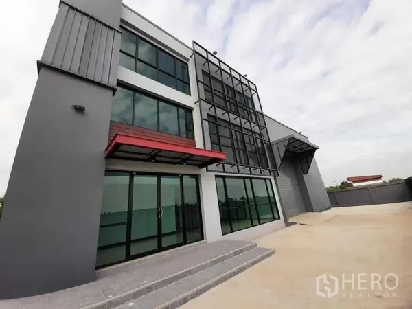 工厂 出租或出售 - 现代三层厂房与办公楼外观，大片玻璃立面与宽阔前院（Lam Luk Ka，巴吞他尼）。