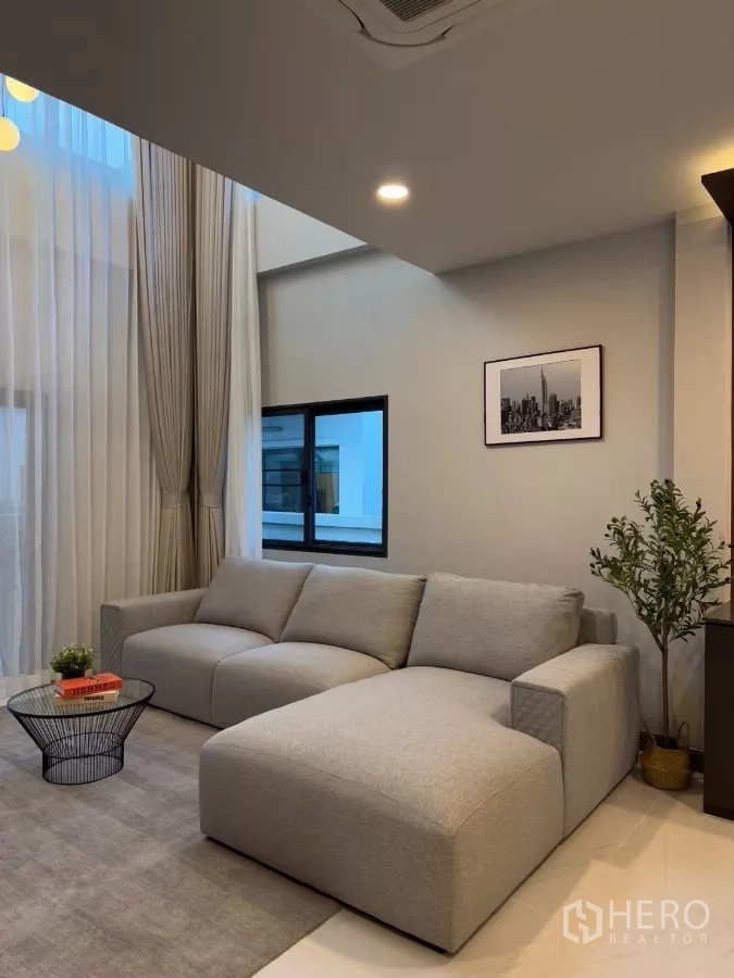 Detached House for rent in Bang Phli, Samut Prakan - Bright living room with double-height ceiling, sheer curtains and gray L-shaped sofa