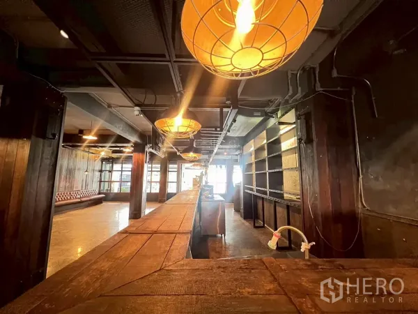 零售空间 出租 - 温暖灯光的室内，设长木吧台、吊灯与内置货架，工业风天花。