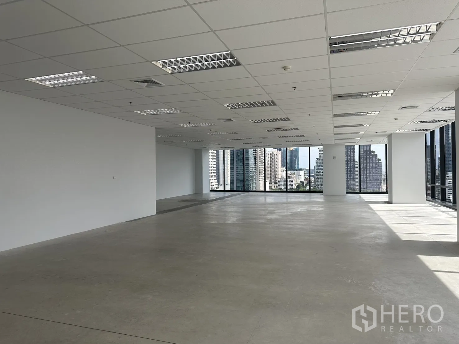 Office Space for rent in Ratchathewi, Bangkok - Bright corner office area with grid ceiling lights, large windows, and polished concrete floor.