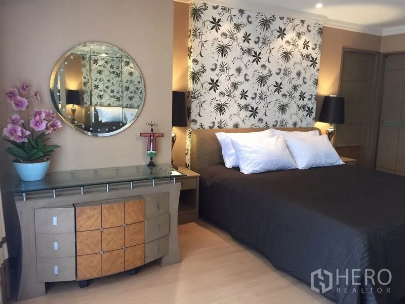 Condominium for rent in Watthana, Bangkok - Bedroom detail showing floral headboard, bedside lamps and dresser with round mirror and orchids.