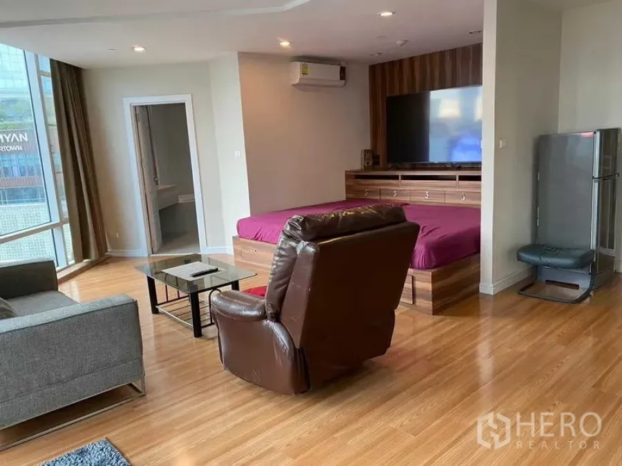 Condominium for rent in Pathum Wan, Bangkok - Spacious corner living space with wood floors, sofa set and city-view glazing.