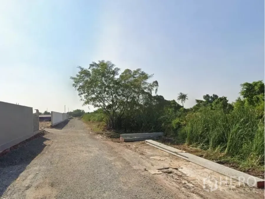 Land for sale in Khlong Toei, Bangkok - Gravel access road beside a boundary wall and trees leading to a vacant land plot under clear sky in Khlong Toei, Bangkok.