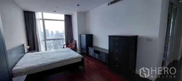 คอนโด ให้เช่าในPathum Wan, Bangkok - ห้องนอนมาสเตอร์ พื้นไม้เข้ม ตู้ลิ้นชักสีดำ เตียงและหน้าต่างบานใหญ่ชมวิวสกายไลน์ปทุมวัน