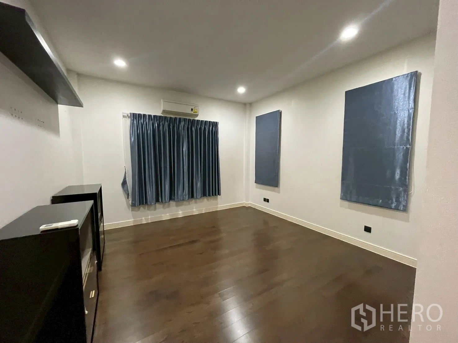 Detached House for rent in Bang Kapi, Bangkok - Large bedroom with wood floors, blue curtains, and wall-mounted shelving.