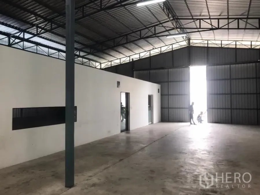 Warehouse for rent in Wang Thonglang, Bangkok - Spacious warehouse interior with steel truss roof, large sliding metal doors, concrete floor and an internal office block.