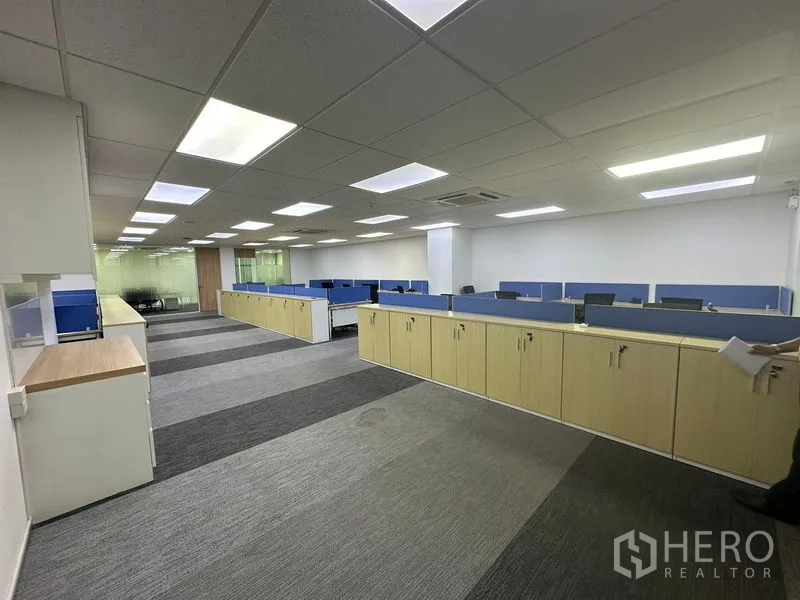 Office Space for rent - Bright open-plan office with blue-partition workstations, ceiling lights and long storage cabinets.
