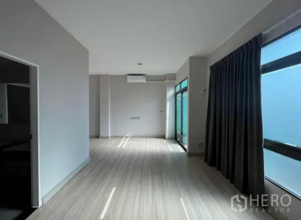 Townhouse for rent or sale in Bang Kho Laem, Bangkok - Bright living room with light wood floors, large windows and blackout curtains in a modern townhouse.