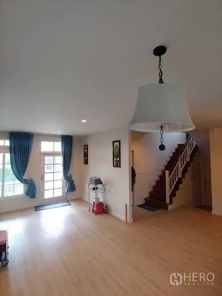 Detached House for sale in Khlong Sam Wa, Bangkok - Spacious living room with light wood flooring, pendant light, and staircase to upper level.