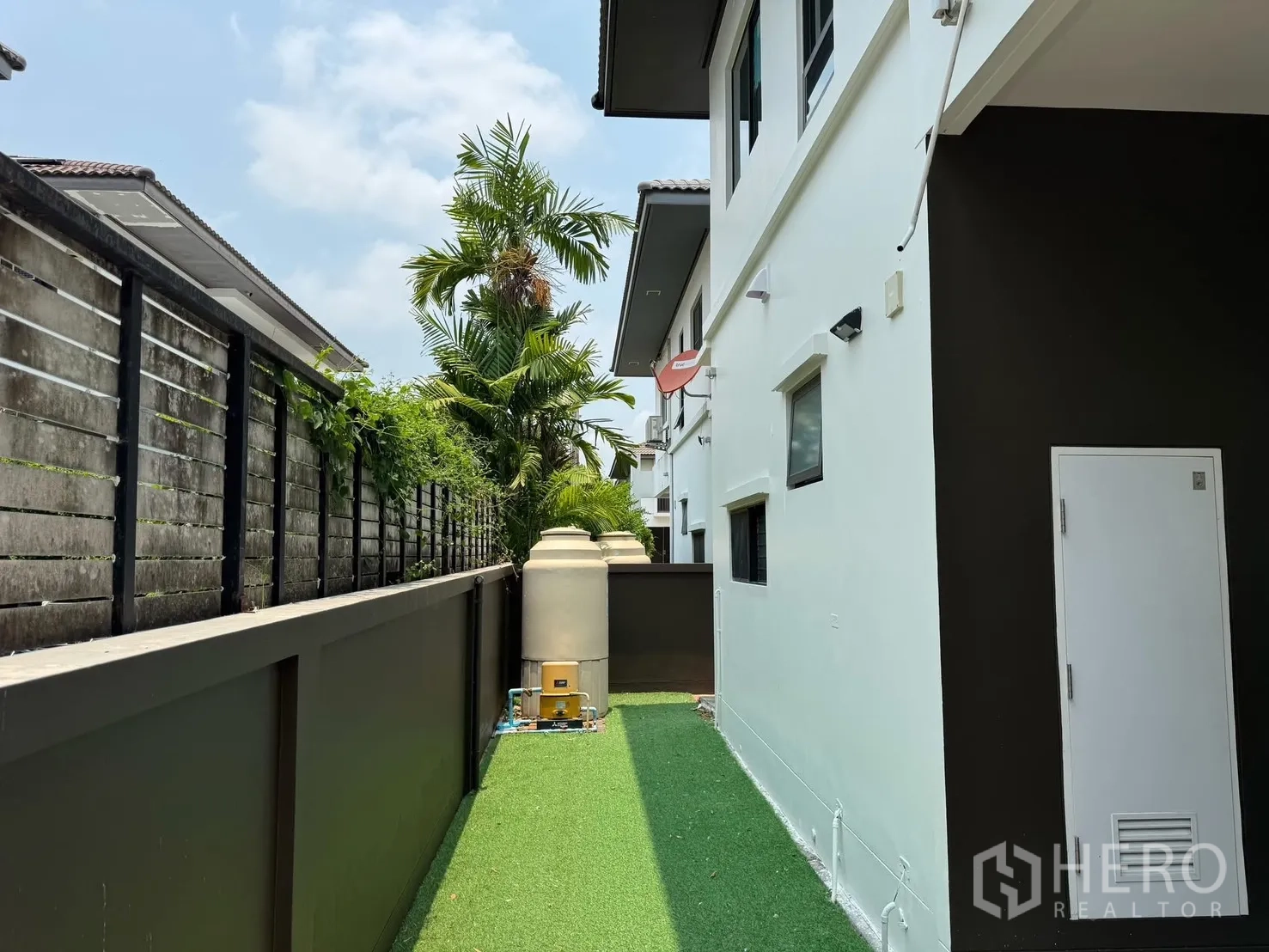 Detached House for rent in Prawet, Bangkok - Narrow side yard with artificial grass, high fence and water tanks.