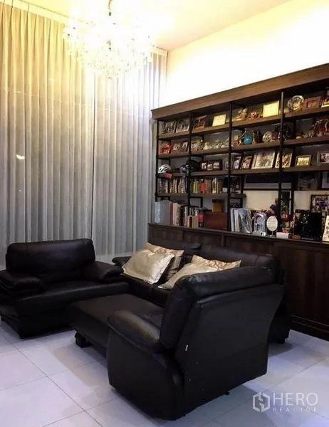 Townhouse for rent in Bang Rak, Bangkok - Cozy sitting area with leather sofas, chandelier lighting, and floor-to-ceiling curtains.