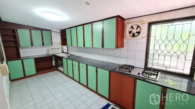 独立式住宅 出租在Lat Phrao, Bangkok - 独立泰式厨房，薄荷绿橱柜、燃气灶、瓷砖墙面与带防盗窗的窗户。